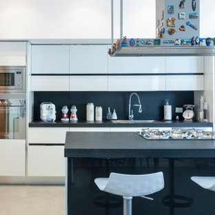 Idee per una cucina design con lavello da incasso, ante lisce, ante bianche, paraspruzzi nero, elettrodomestici in acciaio inossidabile, pavimento grigio e top nero