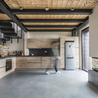 Foto di una cucina a L country con ante lisce, ante in legno chiaro, paraspruzzi nero, elettrodomestici in acciaio inossidabile, pavimento in cemento, nessuna isola, pavimento grigio e top nero