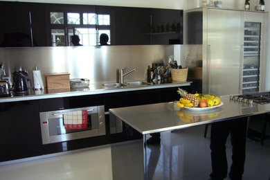 Foto di una cucina design chiusa con lavello a doppia vasca, ante lisce, ante nere, top in acciaio inossidabile, elettrodomestici in acciaio inossidabile, pavimento in marmo e pavimento bianco