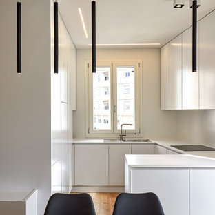Idee per una cucina minimalista di medie dimensioni con lavello da incasso, ante lisce, ante bianche, elettrodomestici in acciaio inossidabile, pavimento in legno massello medio, penisola, pavimento marrone e top bianco