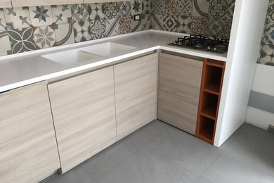 Foto di una grande cucina design con lavello integrato, ante lisce, ante in legno chiaro, top in superficie solida, pavimento in gres porcellanato, penisola, pavimento grigio e top bianco