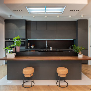 Ispirazione per una cucina design con ante lisce, ante grigie, paraspruzzi nero, elettrodomestici neri, pavimento in legno massello medio e pavimento marrone