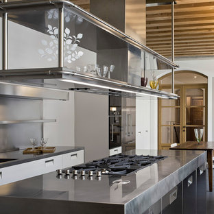 Design ideas for an industrial single-wall eat-in kitchen in Milan with an integrated sink, glass-front cabinets, stainless steel cabinets, stainless steel benchtops, metallic splashback and with island.