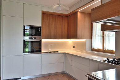 This is an example of a small modern l-shaped open plan kitchen in Other with a double-bowl sink, flat-panel cabinets, white cabinets, composite countertops, stainless steel appliances and white worktops.