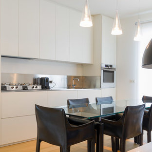 Foto di una cucina lineare design con ante lisce, ante bianche, elettrodomestici in acciaio inossidabile, lavello sottopiano, top in acciaio inossidabile, paraspruzzi grigio, pavimento in legno massello medio, pavimento marrone e top grigio