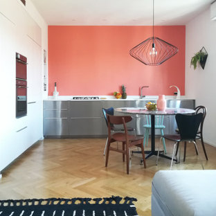 Ispirazione per una cucina design con ante lisce, ante bianche, elettrodomestici in acciaio inossidabile, parquet chiaro, nessuna isola, pavimento beige e top bianco