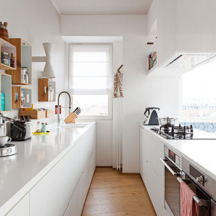 Offene, Zweizeilige, Große Moderne Schmale Küche mit flächenbündigen Schrankfronten, weißen Schränken, Quarzwerkstein-Arbeitsplatte, Küchenrückwand in Weiß, Küchengeräten aus Edelstahl, braunem Holzboden, Halbinsel, braunem Boden und Unterbauwaschbecken in Mailand