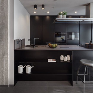 Esempio di una cucina parallela industriale di medie dimensioni con lavello sottopiano, ante lisce, ante nere, top in quarzo composito, elettrodomestici neri, pavimento in gres porcellanato, pavimento grigio, top grigio e penisola