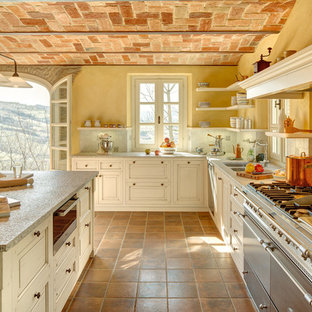 Foto di una grande cucina a L country con top in granito, elettrodomestici in acciaio inossidabile, pavimento in terracotta, isola, lavello a doppia vasca, ante beige, paraspruzzi multicolore e pavimento arancione
