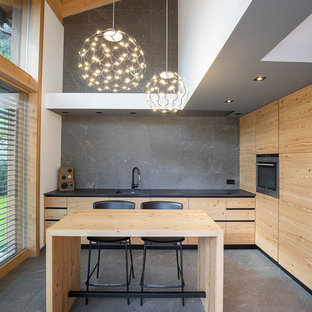 Immagine di un cucina con isola centrale minimal con lavello sottopiano, ante lisce, ante in legno scuro, paraspruzzi grigio, elettrodomestici da incasso, pavimento grigio e top nero