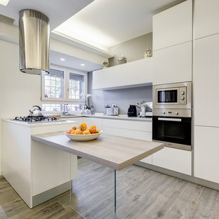 Modelo de cocina comedor en U, minimalista, de tamaño medio, con fregadero integrado, armarios con paneles lisos, salpicadero verde, electrodomésticos de acero inoxidable, suelo laminado, península y suelo gris