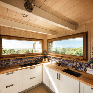 Modelo de cocina en L, de estilo de casa de campo, pequeña, abierta, sin isla, con fregadero bajoencimera, armarios con paneles empotrados, puertas de armario blancas, encimera de madera, salpicadero multicolor, salpicadero de azulejos de cerámica, electrodomésticos de acero inoxidable, suelo de madera pintada, suelo beige y encimeras naranjas