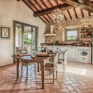 Foto di una cucina mediterranea di medie dimensioni con lavello sottopiano, ante con riquadro incassato, ante bianche, paraspruzzi marrone, paraspruzzi con piastrelle in pietra, elettrodomestici bianchi, pavimento in terracotta, nessuna isola, pavimento marrone, top marrone e soffitto in legno