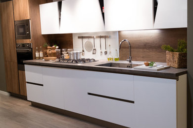 ナポリにある中くらいなモダンスタイルのおしゃれなキッチン (一体型シンク、フラットパネル扉のキャビネット、白いキャビネット、ガラス板のキッチンパネル、シルバーの調理設備、無垢フローリング、茶色いキッチンパネル) の写真