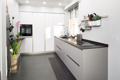 Immagine di una cucina a L design di medie dimensioni e chiusa con pavimento grigio, lavello da incasso, ante lisce, ante grigie, top in superficie solida, elettrodomestici neri, pavimento in gres porcellanato e top nero