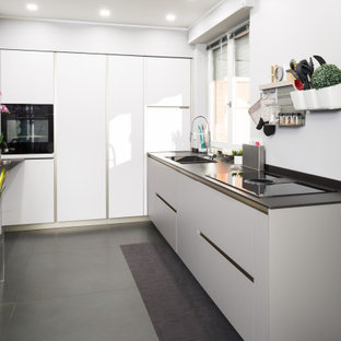 Immagine di una cucina a L design di medie dimensioni e chiusa con pavimento grigio, lavello da incasso, ante lisce, ante grigie, top in superficie solida, elettrodomestici neri, pavimento in gres porcellanato e top nero