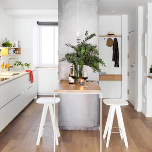 Foto di una cucina parallela minimal con lavello sottopiano, ante lisce, ante bianche, pavimento in legno massello medio, penisola, pavimento marrone e top bianco