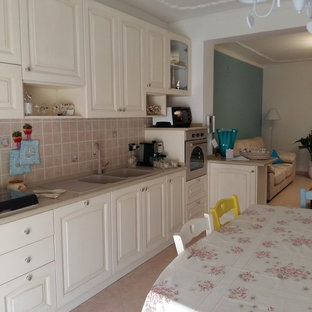 Mid-sized shabby-chic style l-shaped eat-in kitchen in Catania-Palermo with a drop-in sink, recessed-panel cabinets, beige cabinets, quartz benchtops, beige splashback, ceramic splashback, coloured appliances, ceramic floors, a peninsula and orange floor.