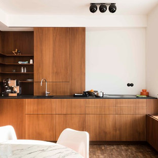 Ispirazione per una cucina design con ante in legno scuro, top nero, lavello sottopiano, ante lisce, paraspruzzi bianco, elettrodomestici da incasso, nessuna isola e pavimento marrone