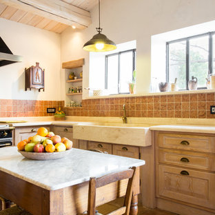Ispirazione per una cucina country con ante con bugna sagomata, ante in legno chiaro, isola, lavello stile country, paraspruzzi rosso, elettrodomestici neri e top beige