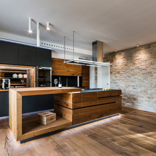 Large contemporary single-wall open plan kitchen in Rome with a drop-in sink, black cabinets, wood benchtops, black splashback, slate splashback, medium hardwood floors, with island and flat-panel cabinets.
