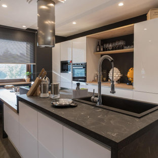 Immagine di una cucina parallela design di medie dimensioni con lavello da incasso, ante lisce, ante bianche, paraspruzzi nero, paraspruzzi in gres porcellanato, elettrodomestici neri, penisola, pavimento grigio e top nero