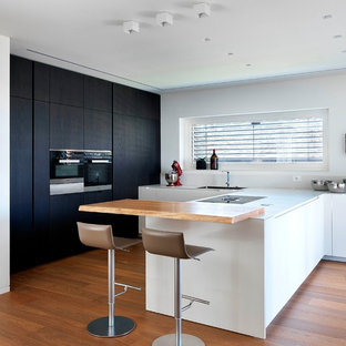 Immagine di una grande cucina a L design con ante lisce, penisola, lavello a vasca singola, ante bianche, elettrodomestici neri, pavimento in legno massello medio e top bianco