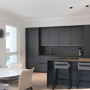 Idee per una cucina parallela minimalista con ante lisce, ante nere, paraspruzzi nero, elettrodomestici da incasso, penisola, pavimento marrone e top grigio