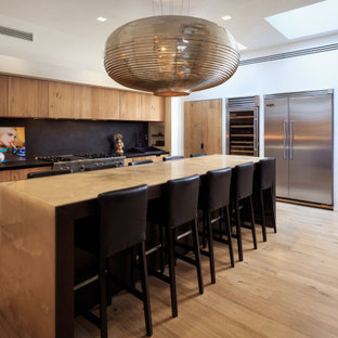 Esempio di una cucina minimal con ante lisce, ante in legno scuro, paraspruzzi nero, elettrodomestici in acciaio inossidabile, parquet chiaro, pavimento beige e top nero