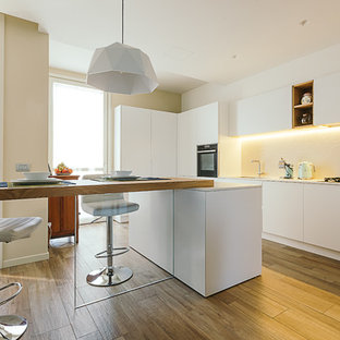 Idee per una cucina minimal con ante bianche, paraspruzzi bianco, lavello sottopiano, ante lisce, elettrodomestici da incasso, pavimento in legno massello medio, pavimento marrone e top bianco