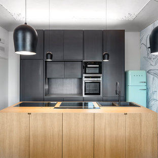 Immagine di una cucina design con lavello da incasso, ante lisce, ante nere, top in legno, paraspruzzi nero, elettrodomestici colorati, pavimento in cementine, isola e pavimento multicolore