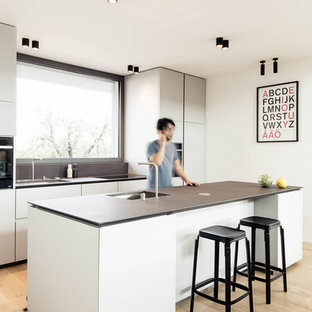 Idee per un cucina con isola centrale moderno di medie dimensioni con lavello sottopiano, top in marmo, parquet chiaro, top nero, ante lisce, ante grigie, paraspruzzi a finestra e pavimento beige