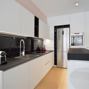 Ispirazione per un cucina con isola centrale design con ante lisce, ante bianche, lavello a vasca singola, paraspruzzi nero, elettrodomestici in acciaio inossidabile, parquet chiaro, pavimento beige e top nero