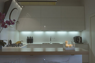 Immagine di una cucina ad U contemporanea chiusa e di medie dimensioni con ante lisce, ante bianche, top in quarzo composito e penisola