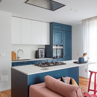 Immagine di una cucina contemporanea di medie dimensioni con lavello da incasso, ante lisce, ante blu, elettrodomestici in acciaio inossidabile, pavimento in legno massello medio, pavimento marrone e top bianco