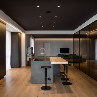 Idee per una cucina moderna con lavello integrato, ante lisce, ante nere, elettrodomestici in acciaio inossidabile, pavimento in legno massello medio, pavimento marrone e top grigio