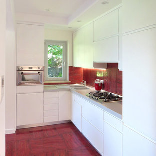 Foto di una cucina a L contemporanea con lavello a doppia vasca, ante lisce, ante bianche, paraspruzzi rosso, elettrodomestici in acciaio inossidabile, nessuna isola, top grigio e pavimento rosso