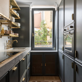 Foto di una cucina ad U tradizionale con lavello integrato, ante nere, paraspruzzi bianco, elettrodomestici neri, pavimento in legno massello medio, nessuna isola, pavimento marrone e top bianco