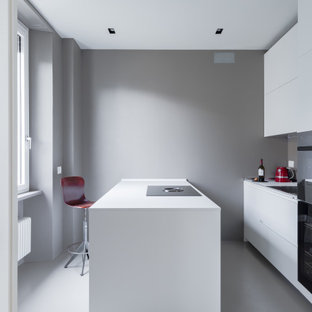 Foto di una cucina parallela moderna con ante lisce, ante bianche, elettrodomestici neri, isola, pavimento grigio e top bianco