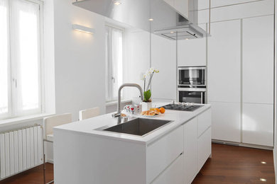 Immagine di una cucina design chiusa e di medie dimensioni con ante lisce, ante bianche, top in quarzo composito, elettrodomestici in acciaio inossidabile, parquet scuro e pavimento marrone