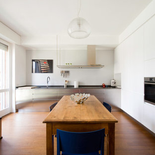 Foto di una cucina minimal con lavello sottopiano, ante lisce, ante bianche, elettrodomestici in acciaio inossidabile, pavimento in legno massello medio, nessuna isola, pavimento marrone e top grigio