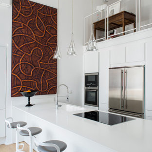 Immagine di una cucina parallela design chiusa e di medie dimensioni con lavello da incasso, ante a filo, ante bianche, top in laminato, parquet chiaro, penisola e top bianco
