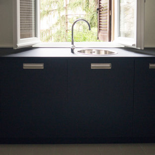 This is an example of a small midcentury l-shaped separate kitchen in Bologna with a drop-in sink, flat-panel cabinets, black cabinets, laminate benchtops, white splashback, black appliances, cement tiles, no island, white floor and black benchtop.