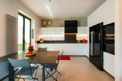 Foto di una cucina design con lavello sottopiano, ante lisce, ante bianche, paraspruzzi nero, elettrodomestici neri, nessuna isola, pavimento bianco e top nero