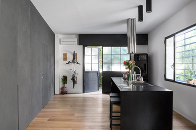 Ejemplo de cocina urbana de tamaño medio con fregadero de un seno, electrodomésticos negros, suelo de madera clara, una isla, suelo beige y encimeras negras
