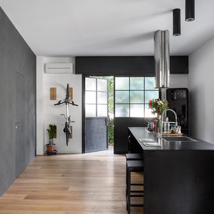 Immagine di un cucina con isola centrale industriale di medie dimensioni con lavello a vasca singola, elettrodomestici neri, parquet chiaro, pavimento beige e top nero