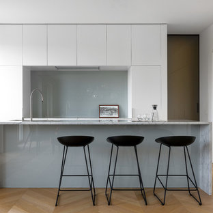 Esempio di una grande cucina moderna con lavello sottopiano, ante lisce, ante bianche, top in marmo, paraspruzzi grigio, paraspruzzi con lastra di vetro, pavimento in legno massello medio, pavimento beige, top bianco e elettrodomestici da incasso