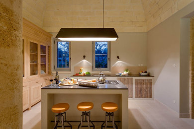 Foto di una cucina mediterranea chiusa con ante con bugna sagomata, ante in legno chiaro, elettrodomestici in acciaio inossidabile, pavimento beige e struttura in muratura