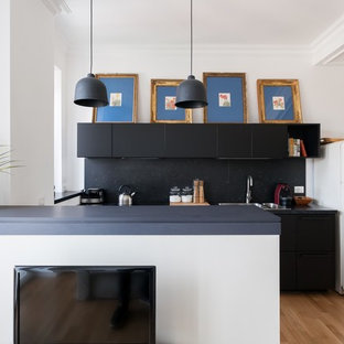 Foto di una cucina parallela moderna con ante lisce, ante nere, paraspruzzi nero, penisola, top nero, lavello da incasso, elettrodomestici bianchi e parquet chiaro