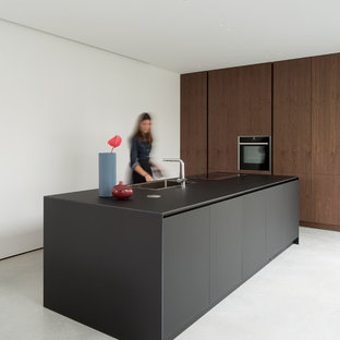 Esempio di un cucina con isola centrale moderno con lavello a vasca singola, ante lisce, ante in legno bruno, elettrodomestici neri, pavimento grigio e top nero